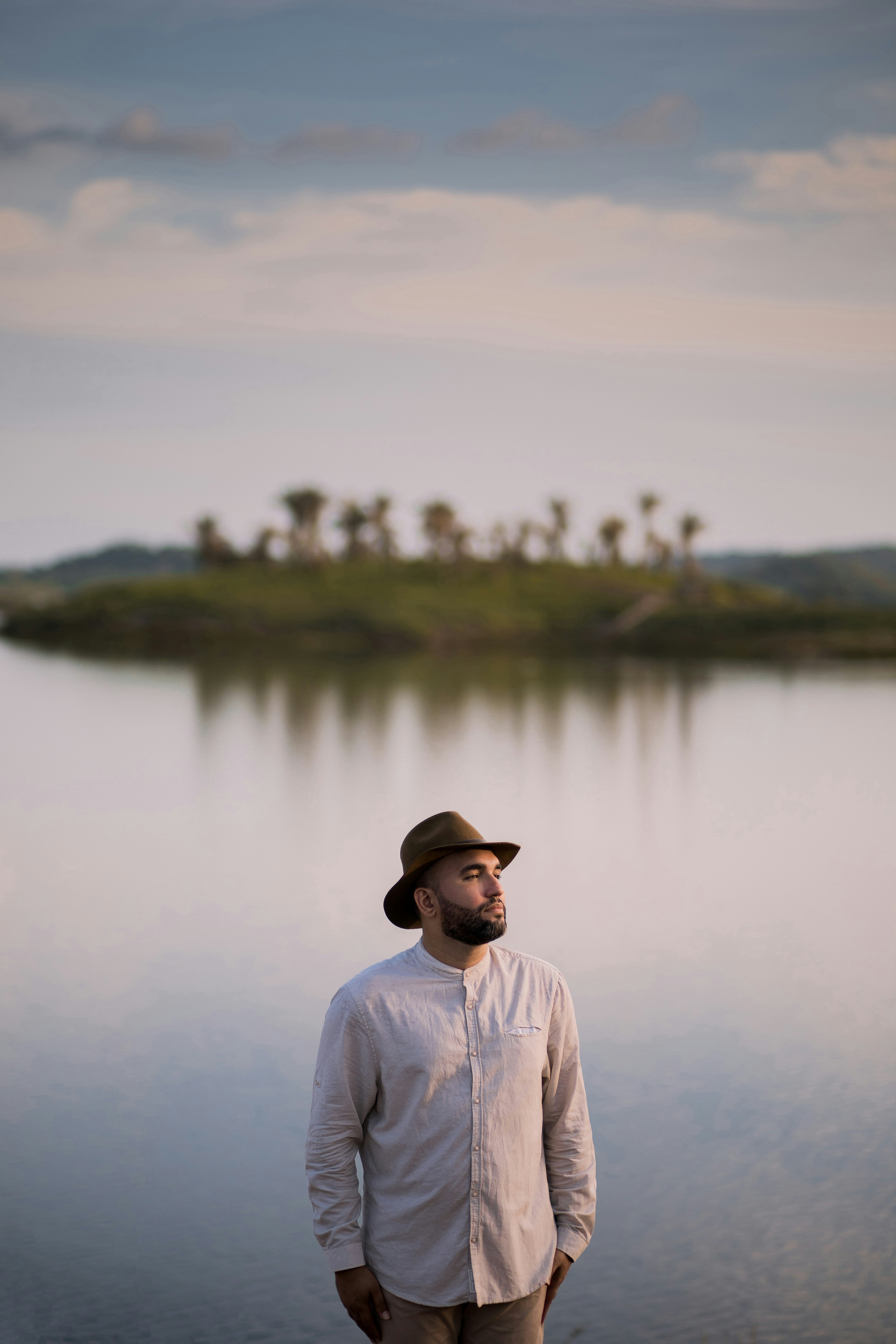 man in white dress shirt wearing black fedora hat standing near lake during daytime